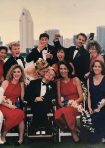 a wedding party group. women in red dresses and men in tuxedos. backdrop of downtown san diego
